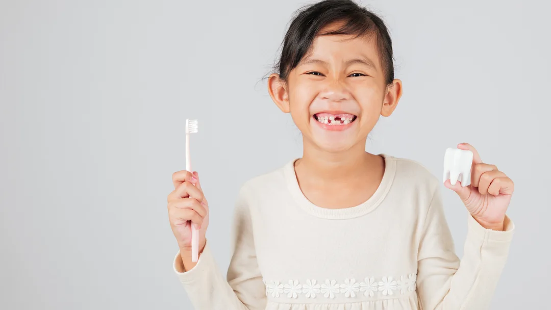 A young patient smiling at Lakewood Dental Group, holding a toothbrush and a model tooth